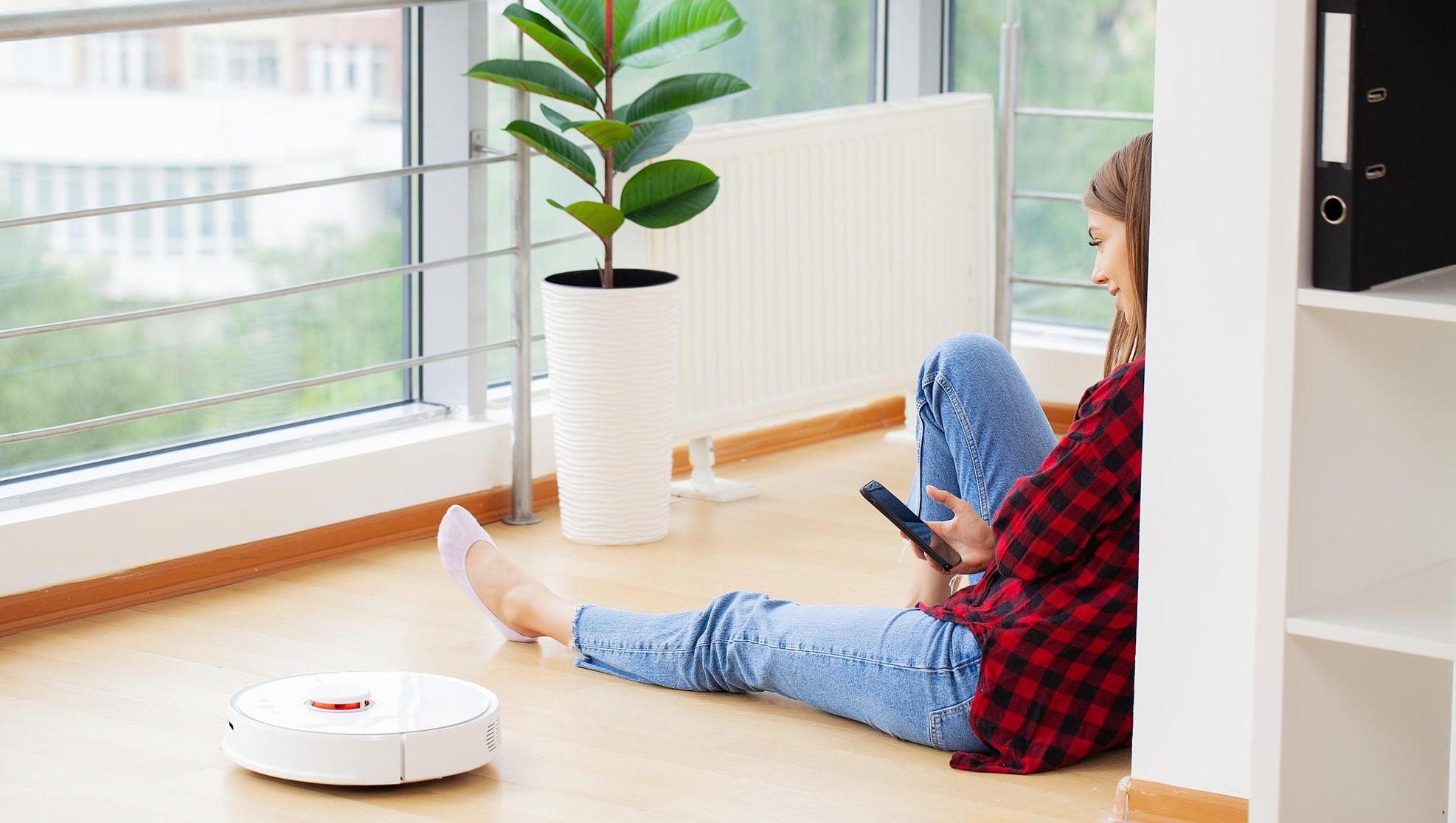 Woman relaxing at home while controlling a smart robot vacuum cleaner with her phone, showcasing HiveCart’s smart home and mini gadget solutions.