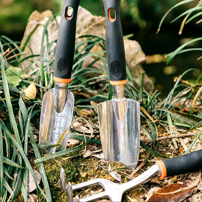 Garden tool set partially inserted in soil with grass and rocks in the background