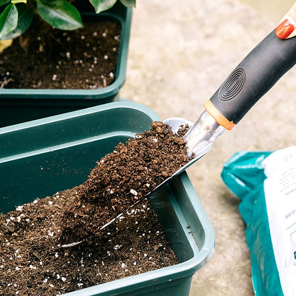 Close-up of a hand using a garden trowel to scoop soil into a green planter box
