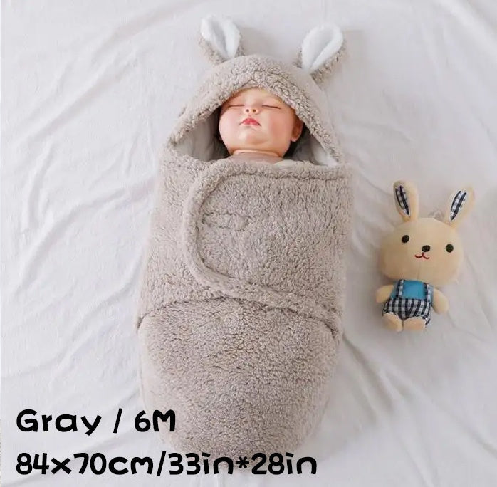 Baby wrapped in a gray fluffy swaddle sleeping bag with bunny ears, size 6M