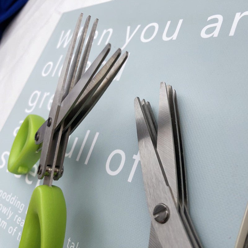 Close-up of multi-layer herb scissors with green handles on a blue background.