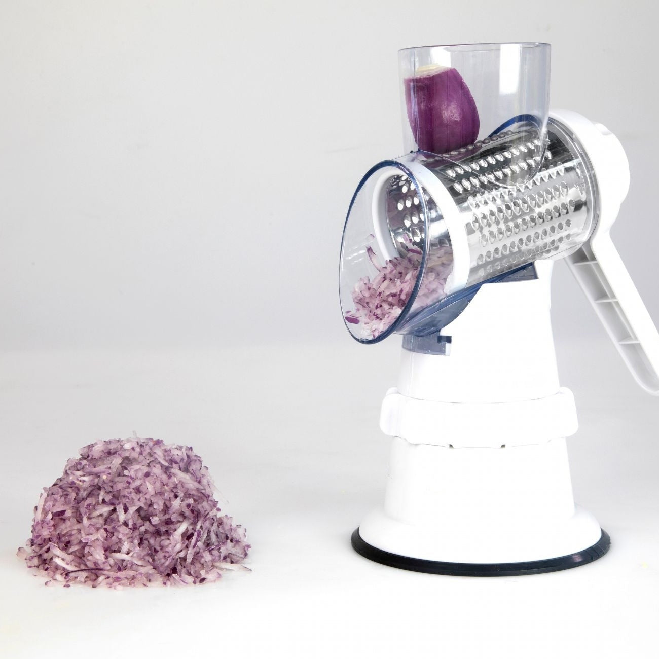 Manual vegetable grater shredding purple onion on white surface with rotary blade.