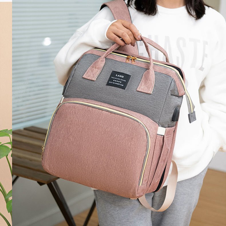 Mom holding pink and gray mummy baby crib backpack in a cozy home setting