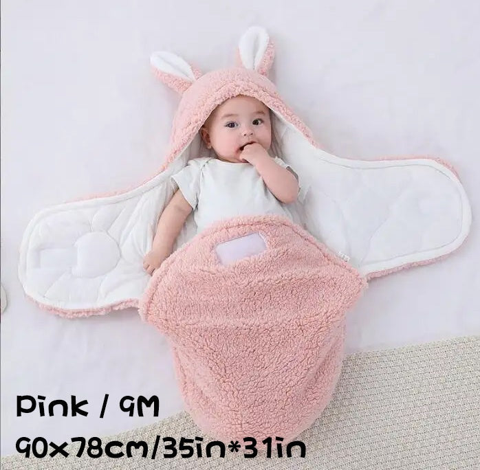 Baby wearing a pink fluffy swaddle sleeping bag with bunny ears, labeled Pink / 9M, 90×78cm / 35in×31in