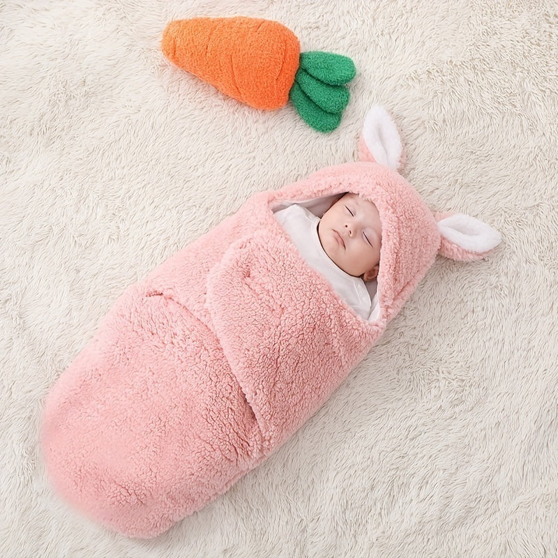 A sleeping baby wrapped in a pink fluffy swaddle sleeping bag with bunny ears, lying on a soft cream-colored rug.