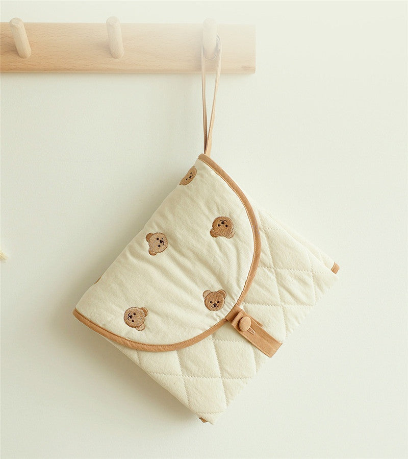 Portable baby changing pad with bear pattern, folded and hanging on a wooden hook