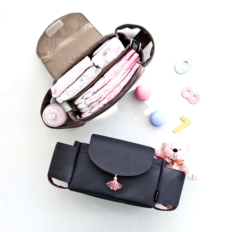 Flatlay of two stroller organizer bags, one open showing diapers, baby clothes, and a bottle, the other closed with a plush toy inside, surrounded by baby toys on a white surface.