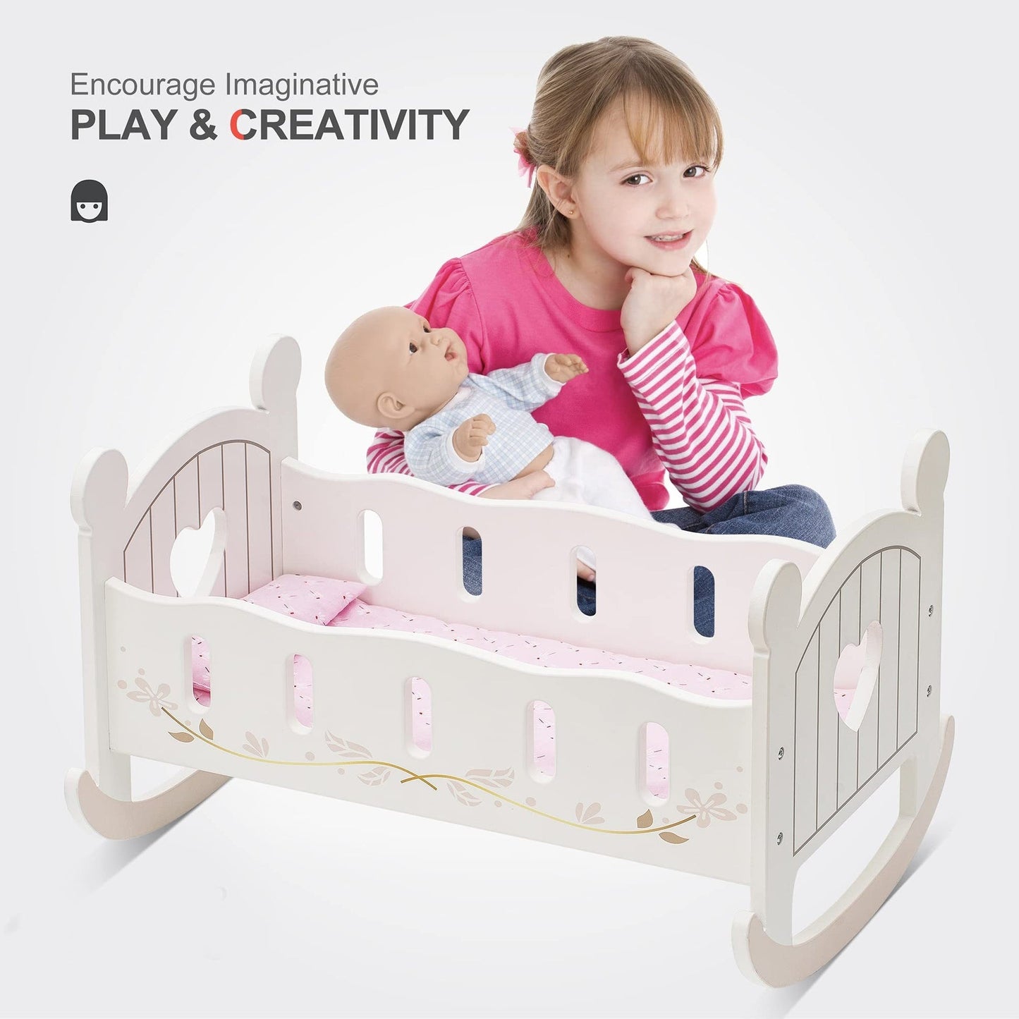 Smiling girl holding a doll next to a wooden rocking cradle with heart cutouts and pink bedding