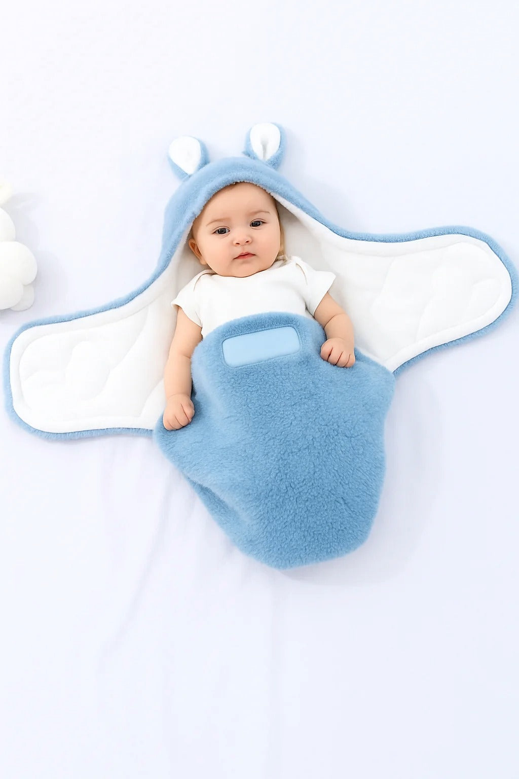 Baby wrapped in a soft blue swaddle with bunny ears, lying on a white blanket.
