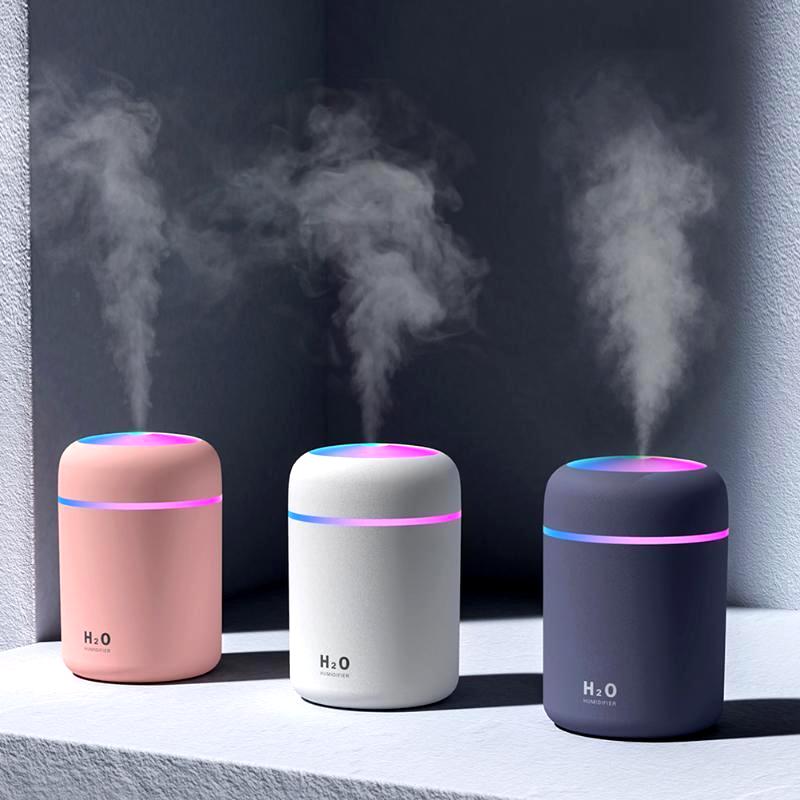 Three colorful USB air humidifiers—pink, white, and navy—emitting cool mist on a modern surface, with LED light accents