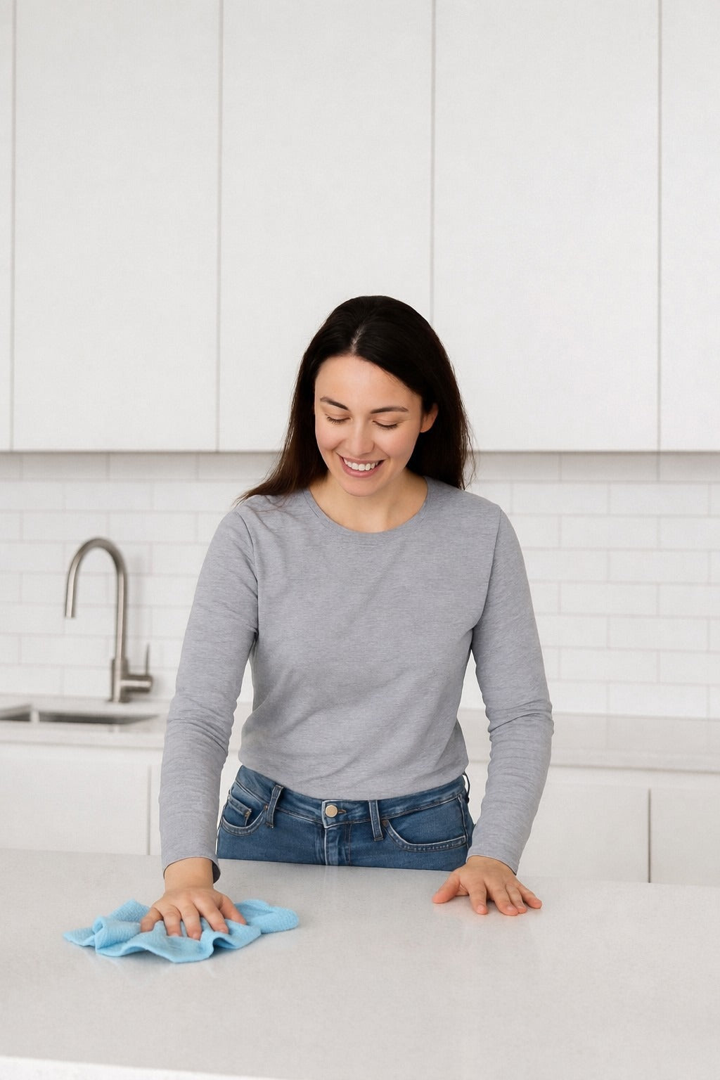 Woman wiping a kitchen counter with a blue microfiber cloth in a bright modern kitchen during a quick daily cleaning routine.