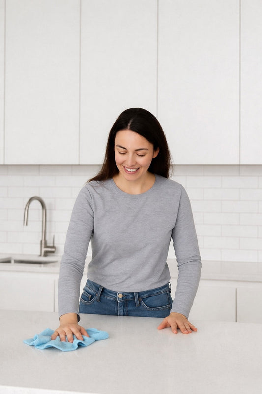 Woman wiping a kitchen counter with a blue microfiber cloth in a bright modern kitchen during a quick daily cleaning routine.