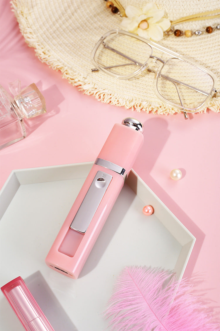 A pink nano facial mister displayed on a tray with sunglasses, perfume, and accessories, representing daily skincare on the go