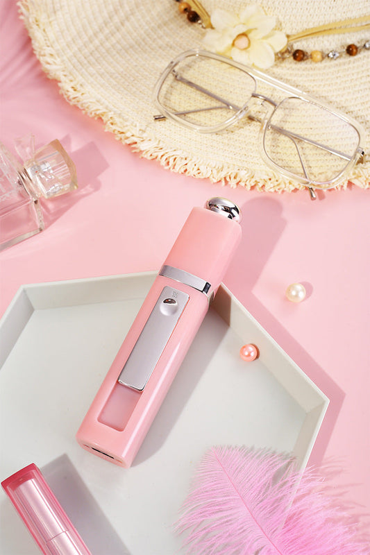 A pink nano facial mister displayed on a tray with sunglasses, perfume, and accessories, representing daily skincare on the go