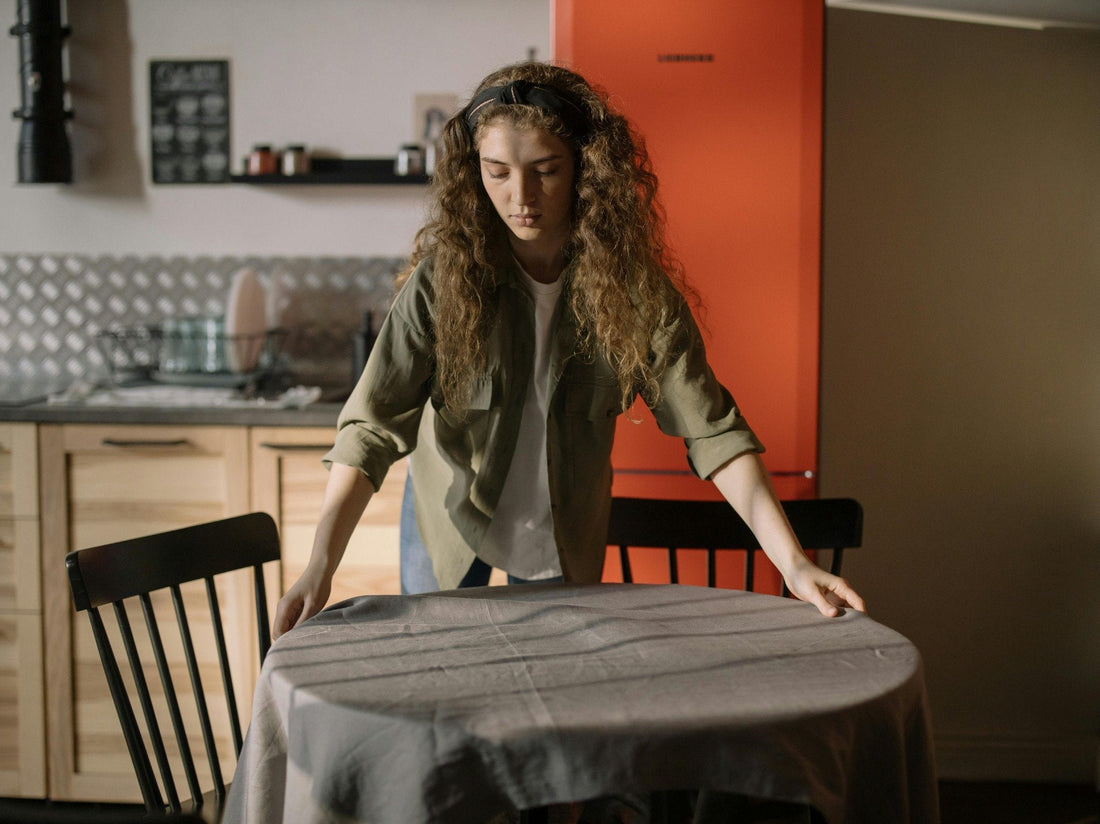 Woman in a cozy kitchen setting adjusting a tablecloth, creating a calm and tidy atmosphere that reflects a peaceful end-of-day cleaning routine.