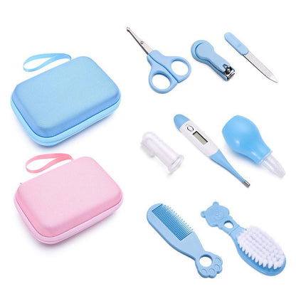 Flat lay of baby grooming kit with blue and pink travel cases, scissors, nail clippers, digital thermometer, nasal aspirator, finger toothbrush, brush, and comb