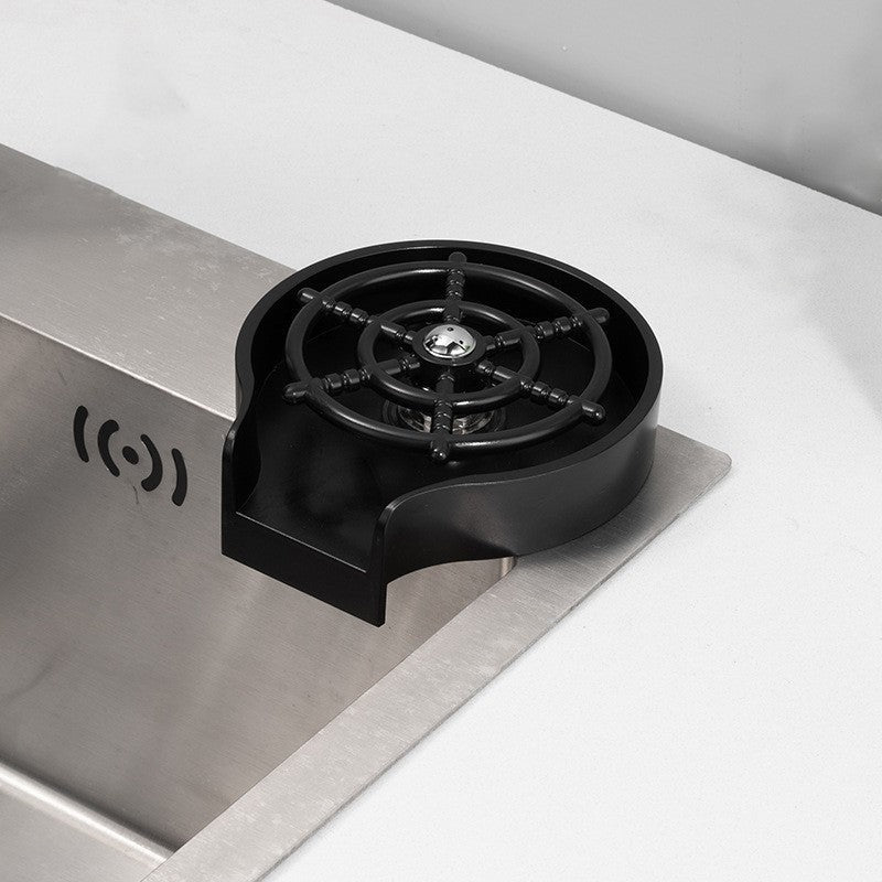 Black glass rinser device installed next to a stainless steel kitchen sink on a white countertop.
