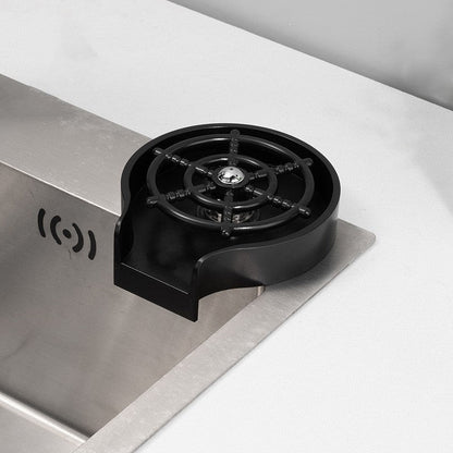 Black glass rinser device installed next to a stainless steel kitchen sink on a white countertop.