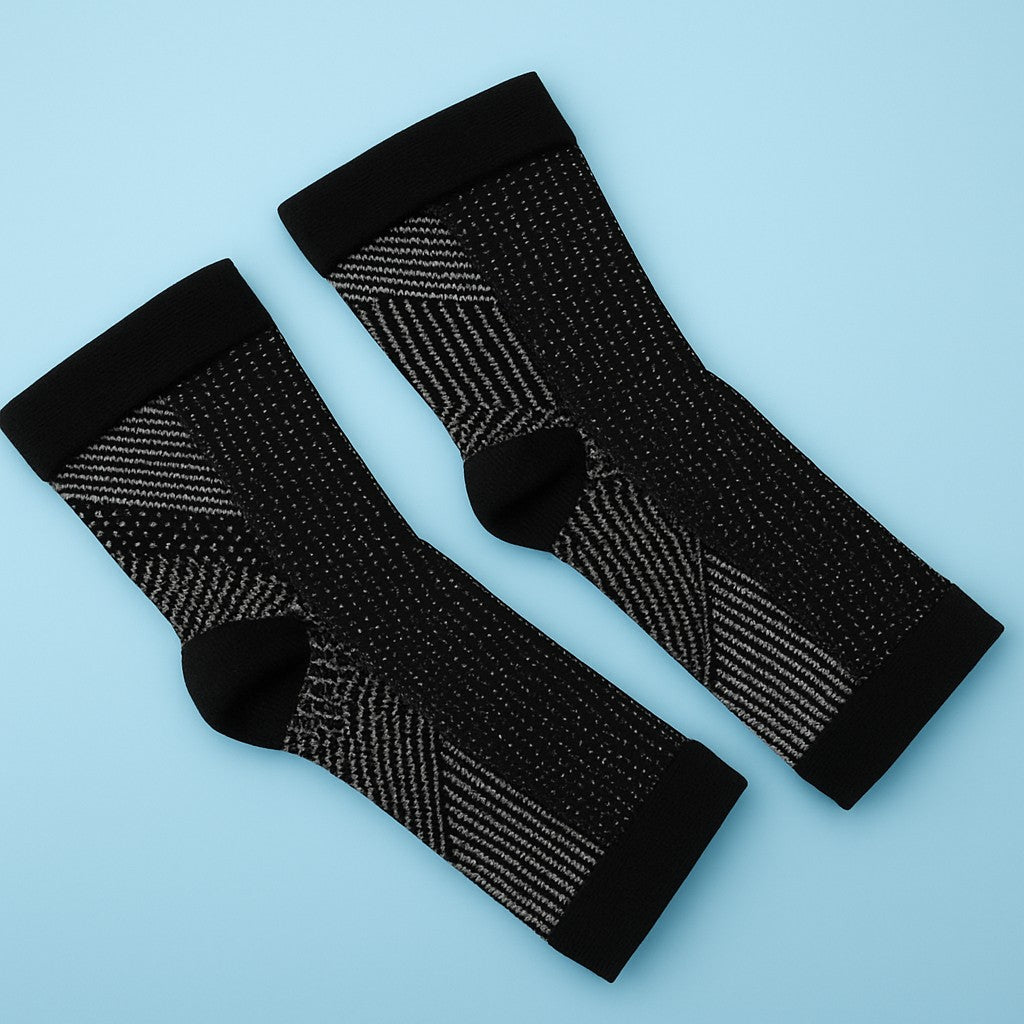 Pair of black compression ankle sleeves with white woven patterns, laid flat on a light blue background for product display