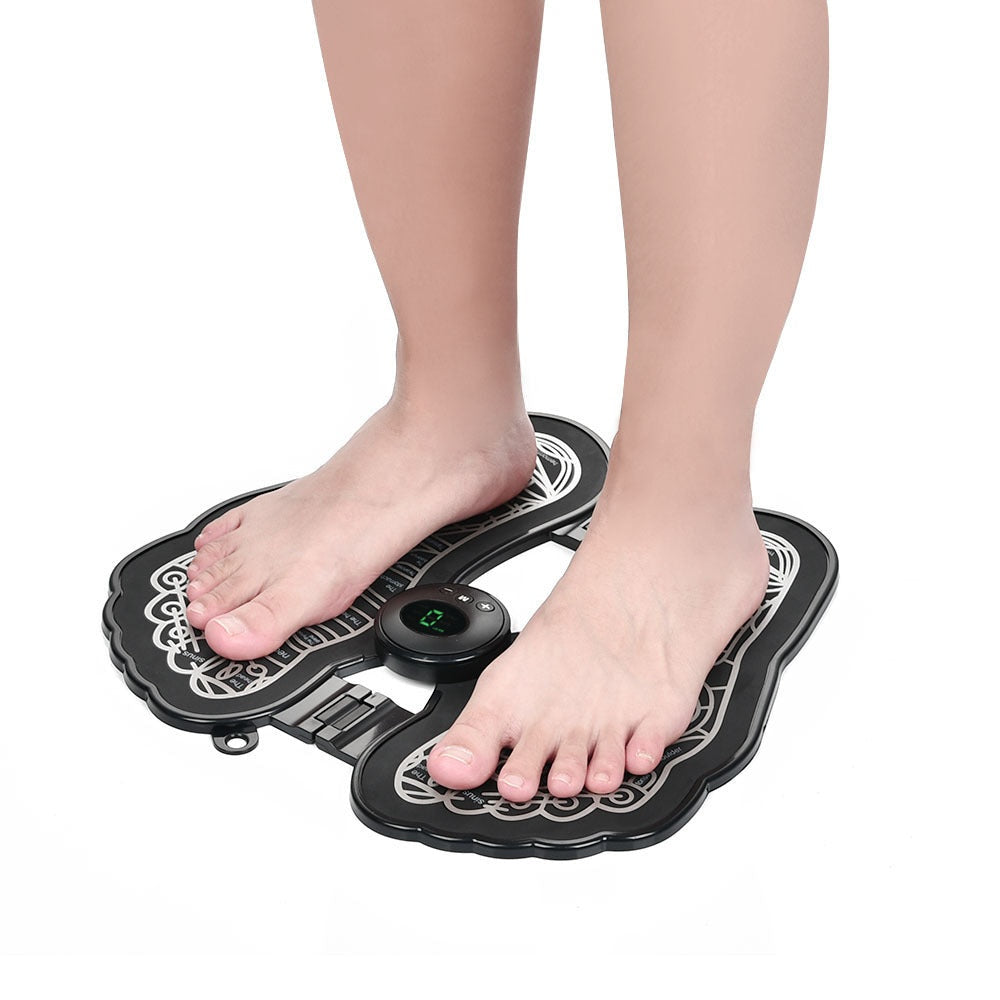 A person standing on an EMS foot massager pad with a digital control unit in the center.