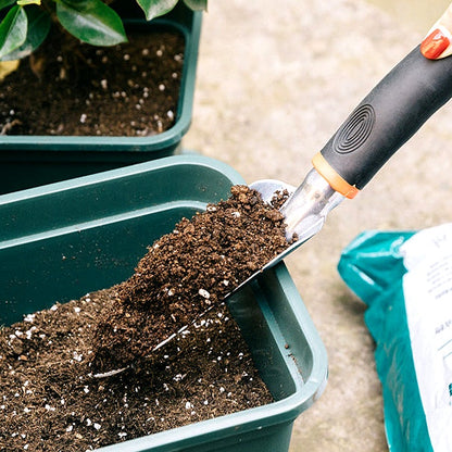 Close-up of a hand using a garden trowel to scoop soil into a green planter box
