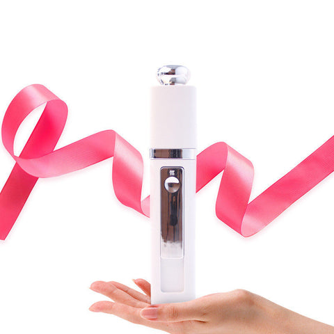 White nano mist sprayer held above a hand with a pink ribbon background