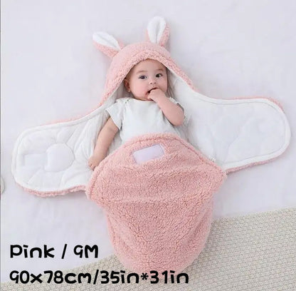 Baby wearing a pink fluffy swaddle sleeping bag with bunny ears, labeled Pink / 9M, 90×78cm / 35in×31in