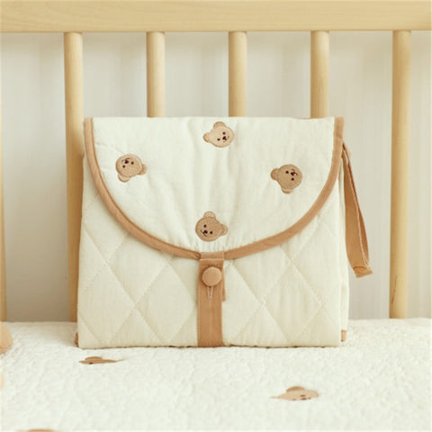 Portable baby changing pad with bear pattern, folded and placed on crib