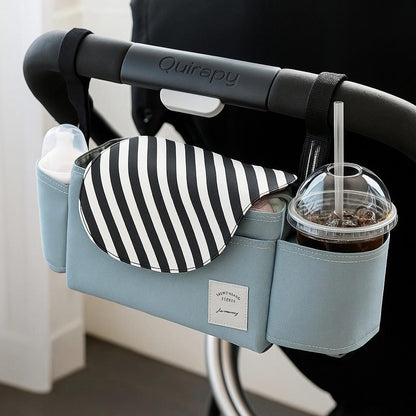 Stroller organizer bag attached to a stroller handle, featuring a striped flap, baby bottle holder, and cup holder with iced drink.