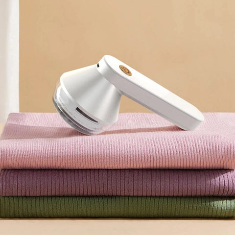 White USB rechargeable electric lint remover resting on folded sweaters in pastel colors.